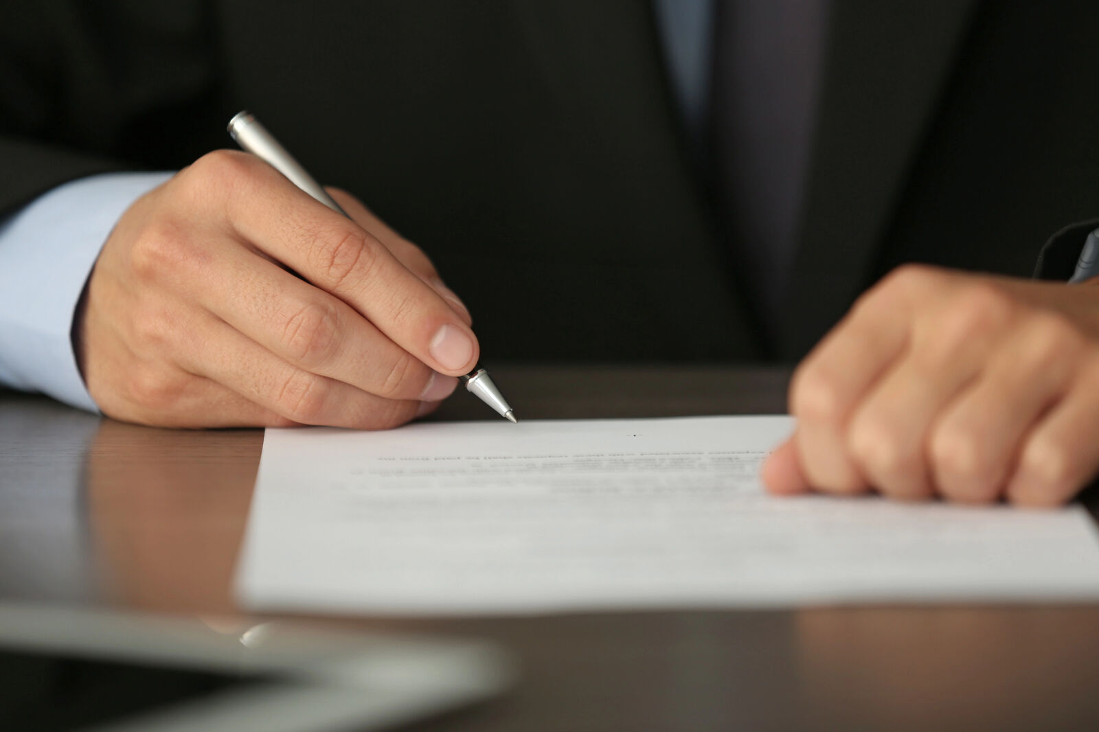 Close-up of a man in a suit using a pen to edit a paper.