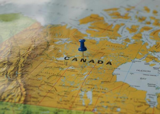 A blue pushpin stuck in the middle of Canada on a map of the world