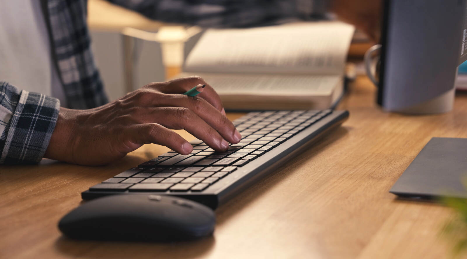 A hand clutches a pencil while resting on a black computer keyboard.