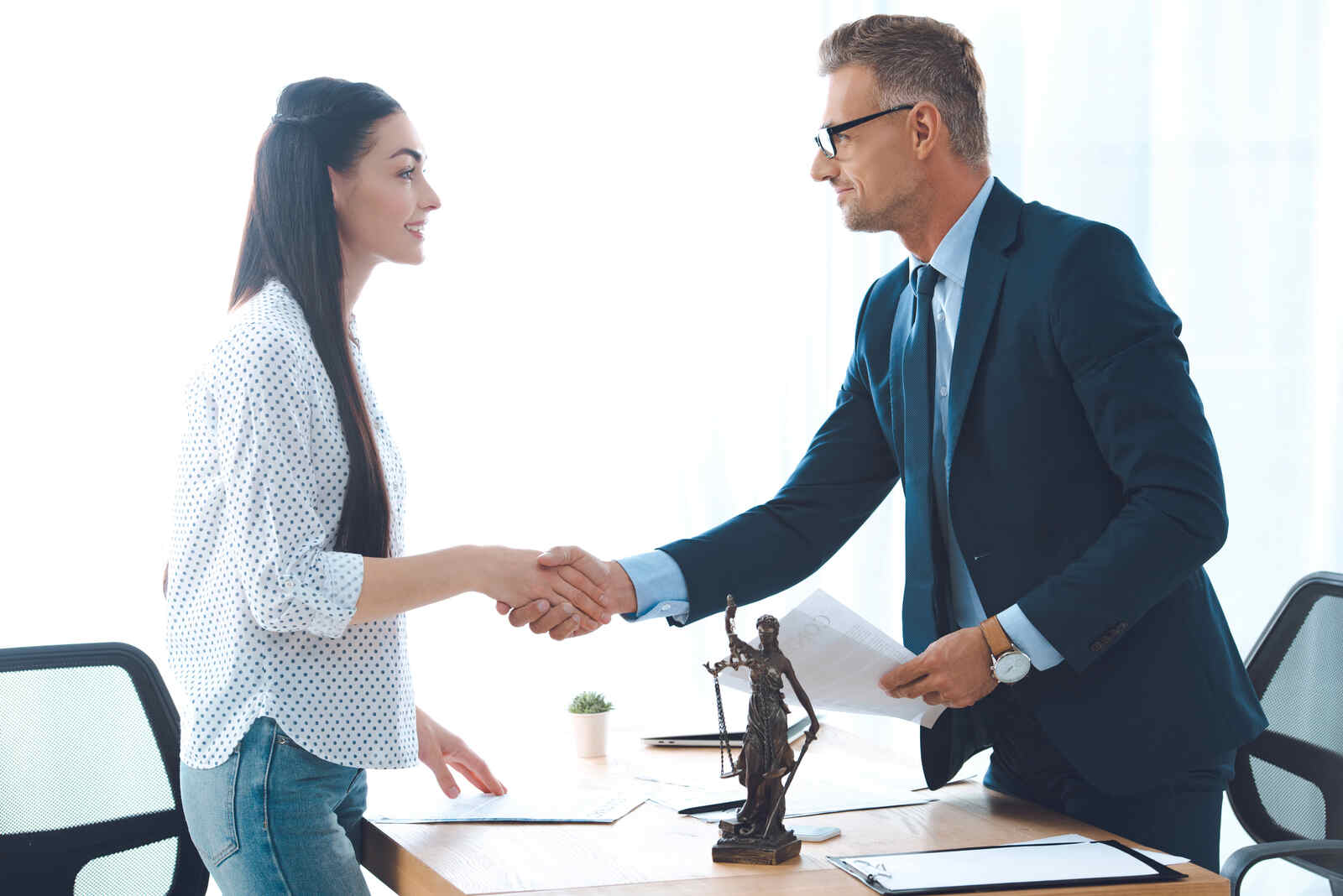 Side view of professional lawyer and young female client shaking hands.