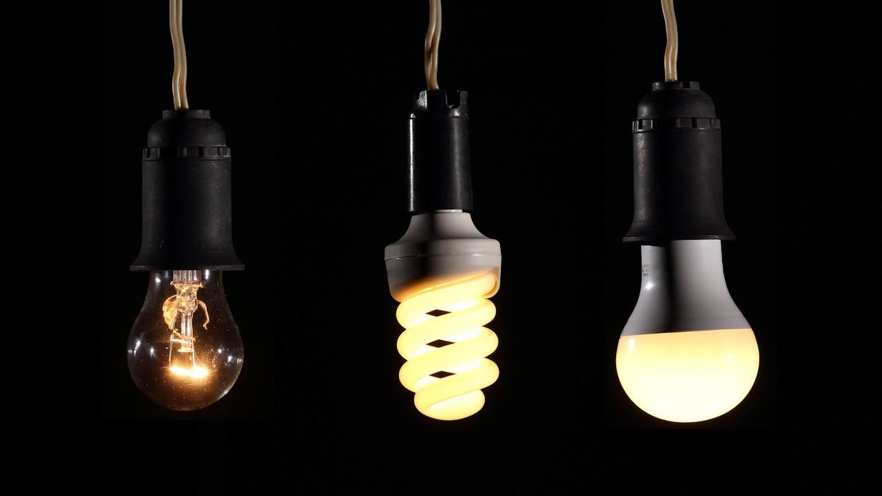 Three different types of lightbulb hang side-by-side, with each one notably brighter than the last.