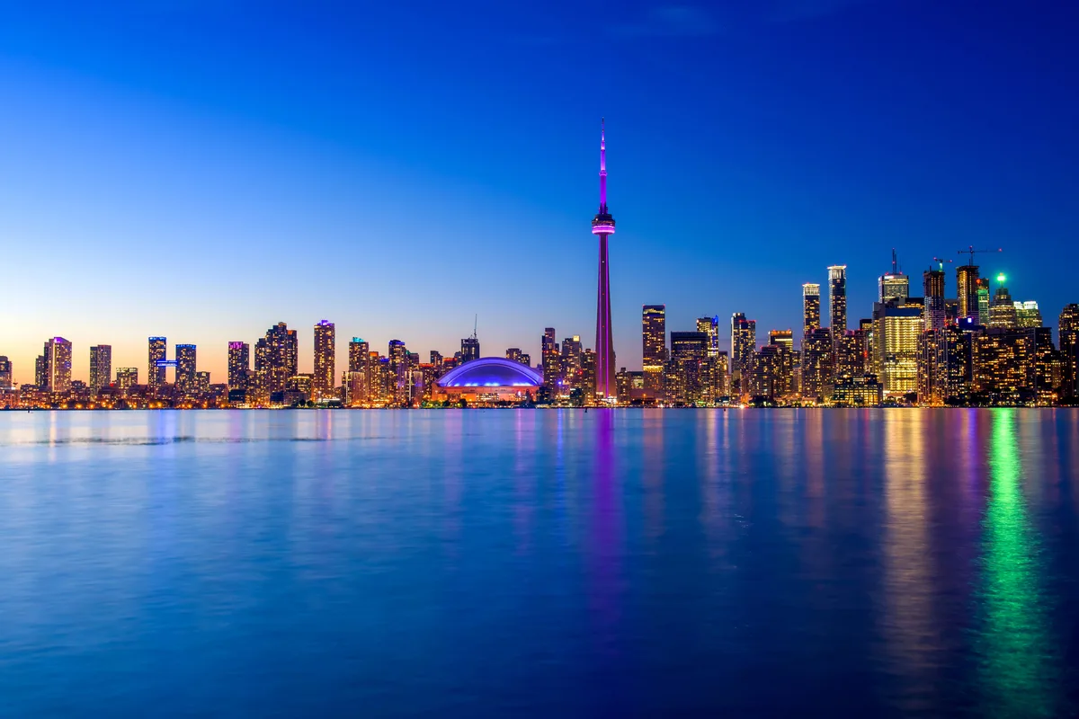 The Toronto skyline at dusk, with the CN Tower lit purple above Lake Ontario