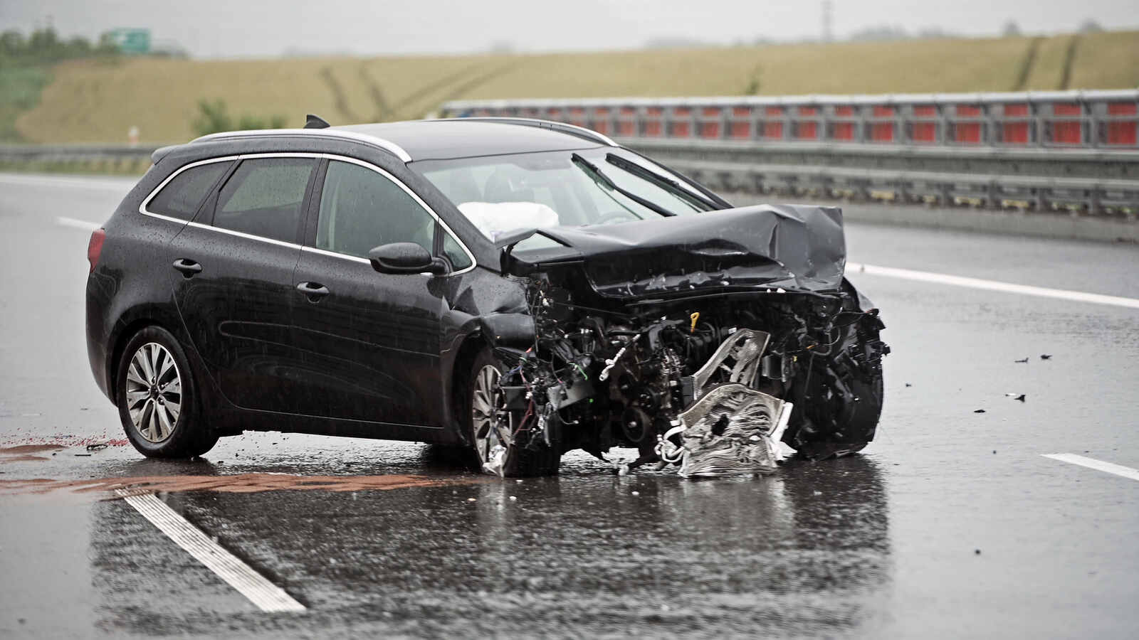 A black SUV with a badly damaged front-end sits on the highway during a heavy rain.