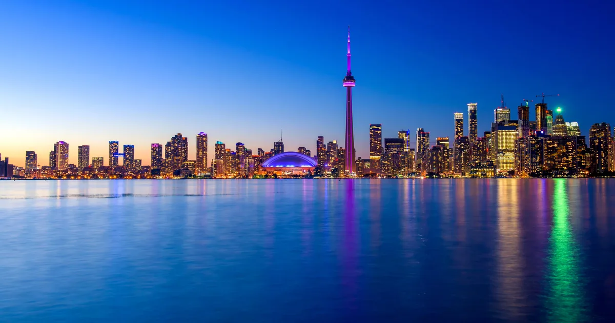 The Toronto skyline at dusk, with the CN Tower lit purple above Lake Ontario
