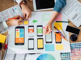 Top-down view of web designers reviewing mobile phone interfaces for website user experience designs