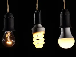 Three different types of lightbulb hang side-by-side, with each one notably brighter than the last.